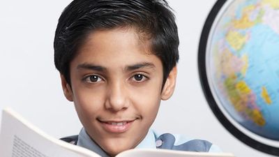 Young boy with an open book looking at the camera and a globe at his side (East India, asian, student, education).